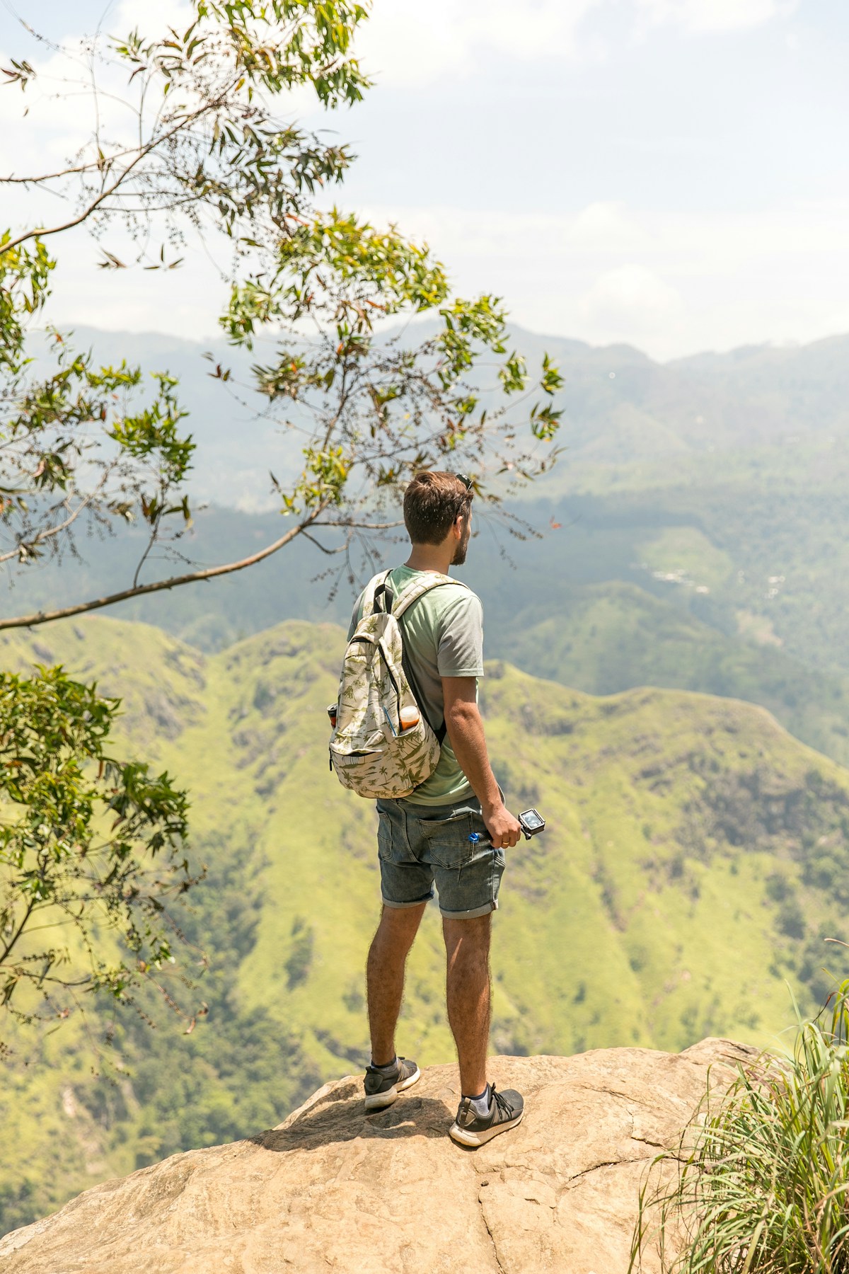Traveller with backpack standing on a hilltop looking over green Sri Lankan hill country near Ella