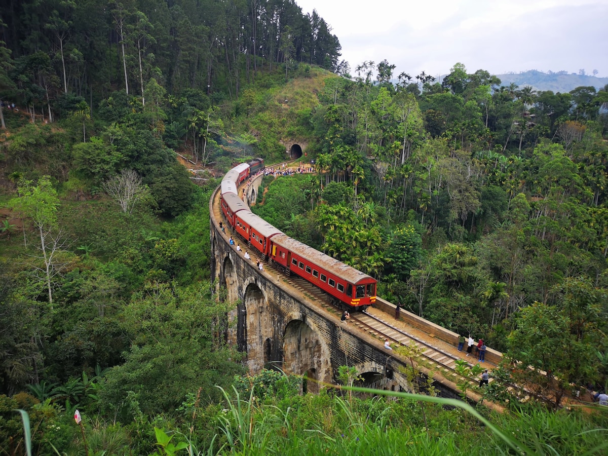 Red train crossing Nine Arches Bridge through lush forest, Ella, Sri Lanka