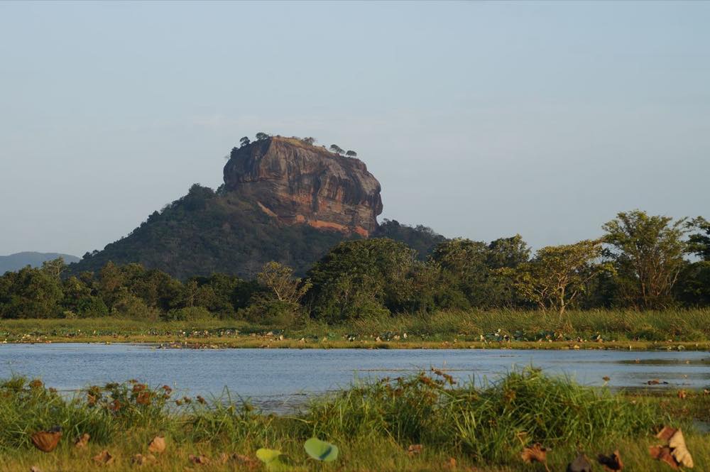 Sigiriya Rock rising above the forest and lake at sunrise