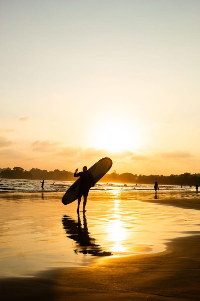 Surfer mit Brett am Strand von Weligama bei Sonnenuntergang