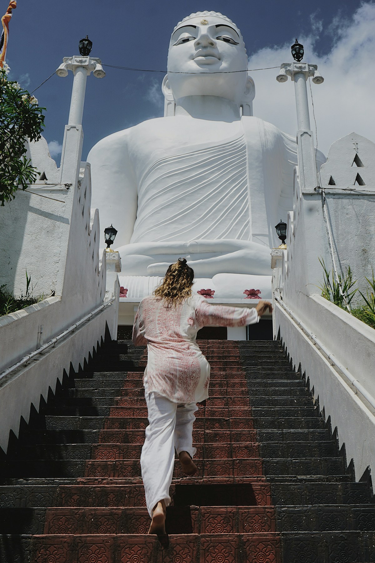 Woman climbing stairs toward giant Buddha statue, Kandy, Sri Lanka