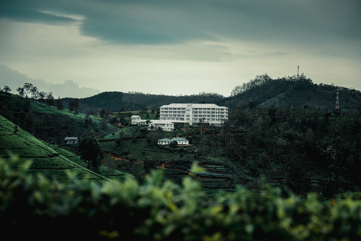 Large white hotel building on a lush green hillside among tea plantation terraces, Sri Lanka