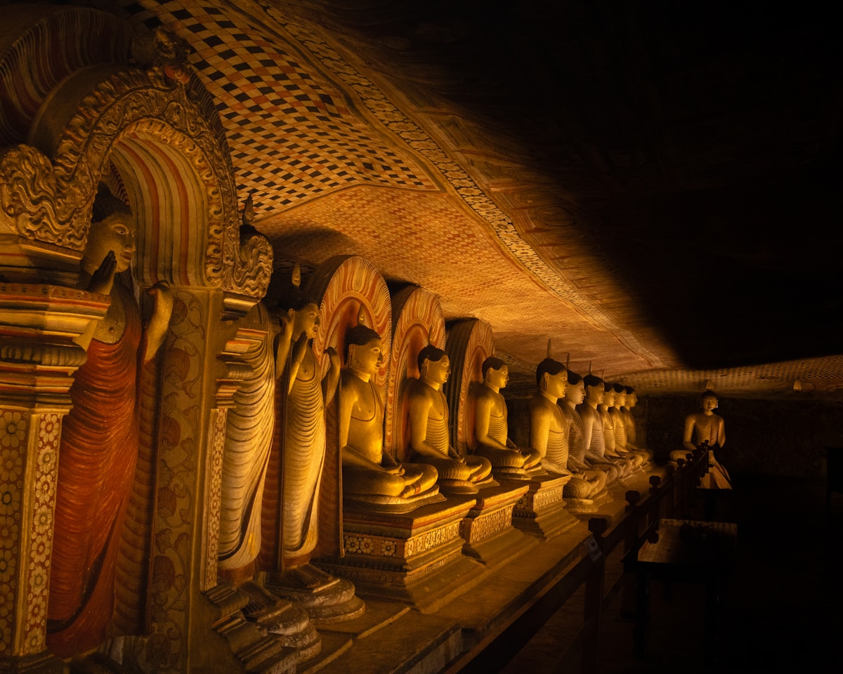 Row of golden Buddha statues in a dimly lit cave, Dambulla Cave Temple, Sri Lanka