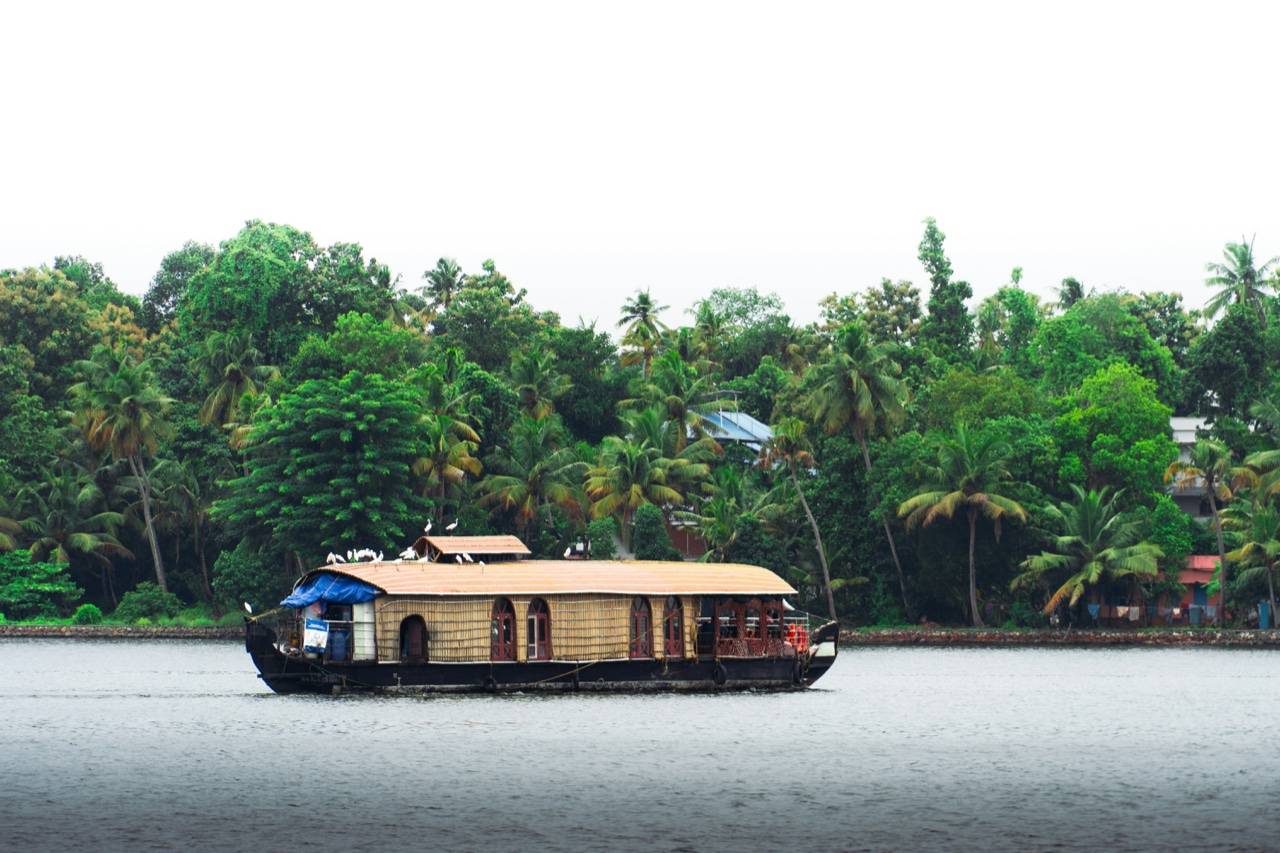 Kerala backwaters with traditional wooden houseboat gliding through palm-fringed canals, southern India
